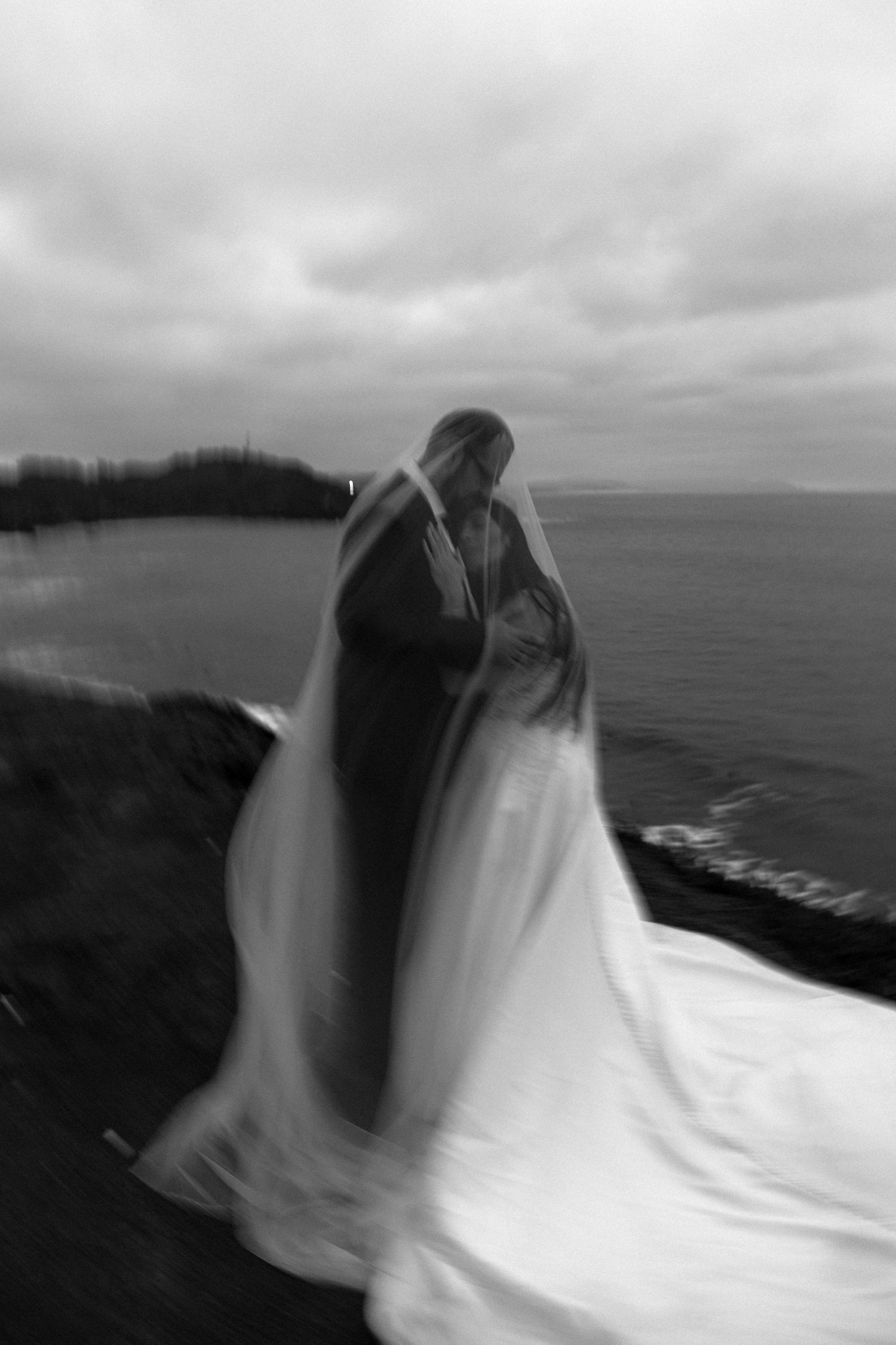 Ethereal black and white coastal scene with flowing white fabric against a cloudy ocean backdrop.
