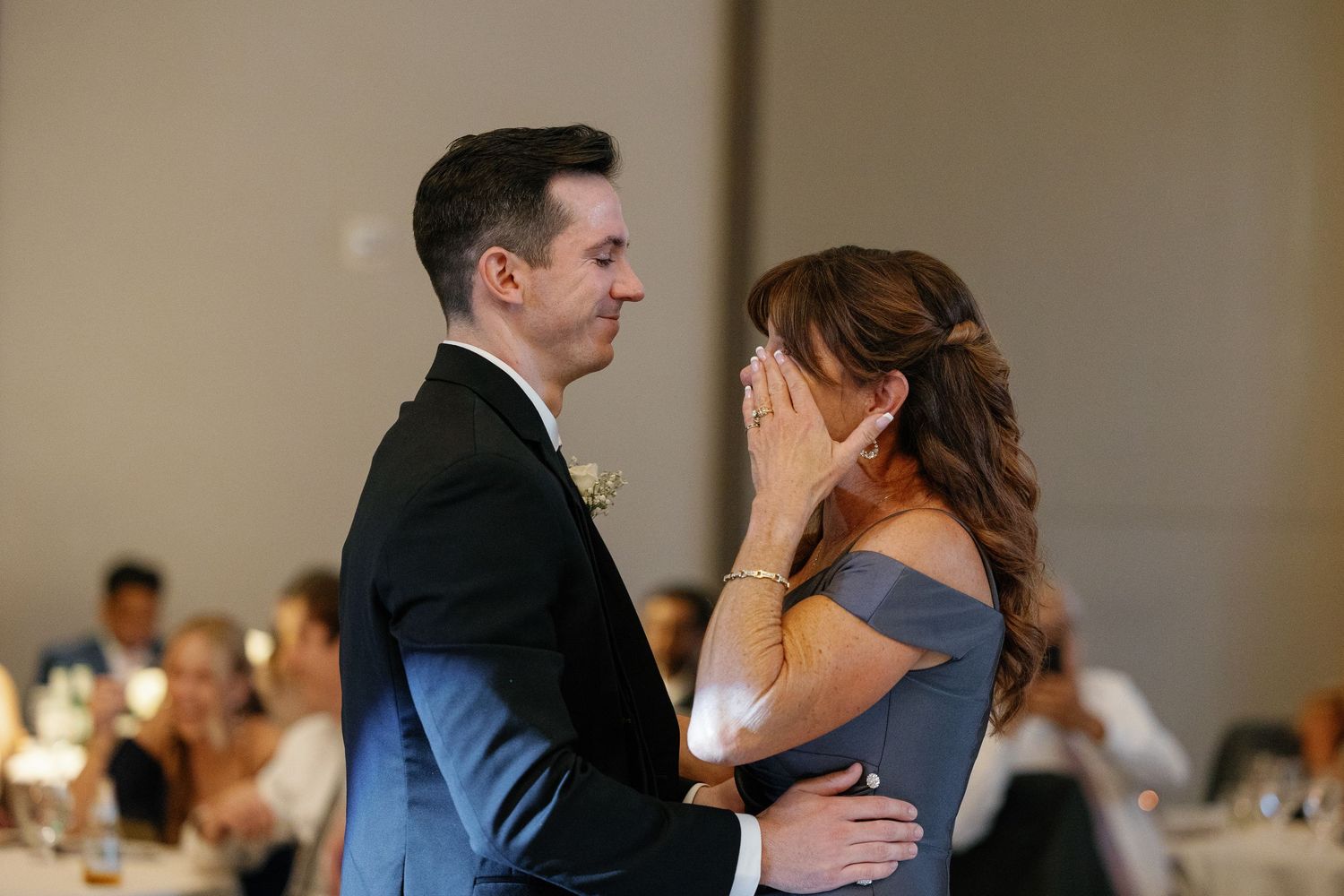 A couple shares an intimate dance at a wedding reception in a softly lit ballroom.