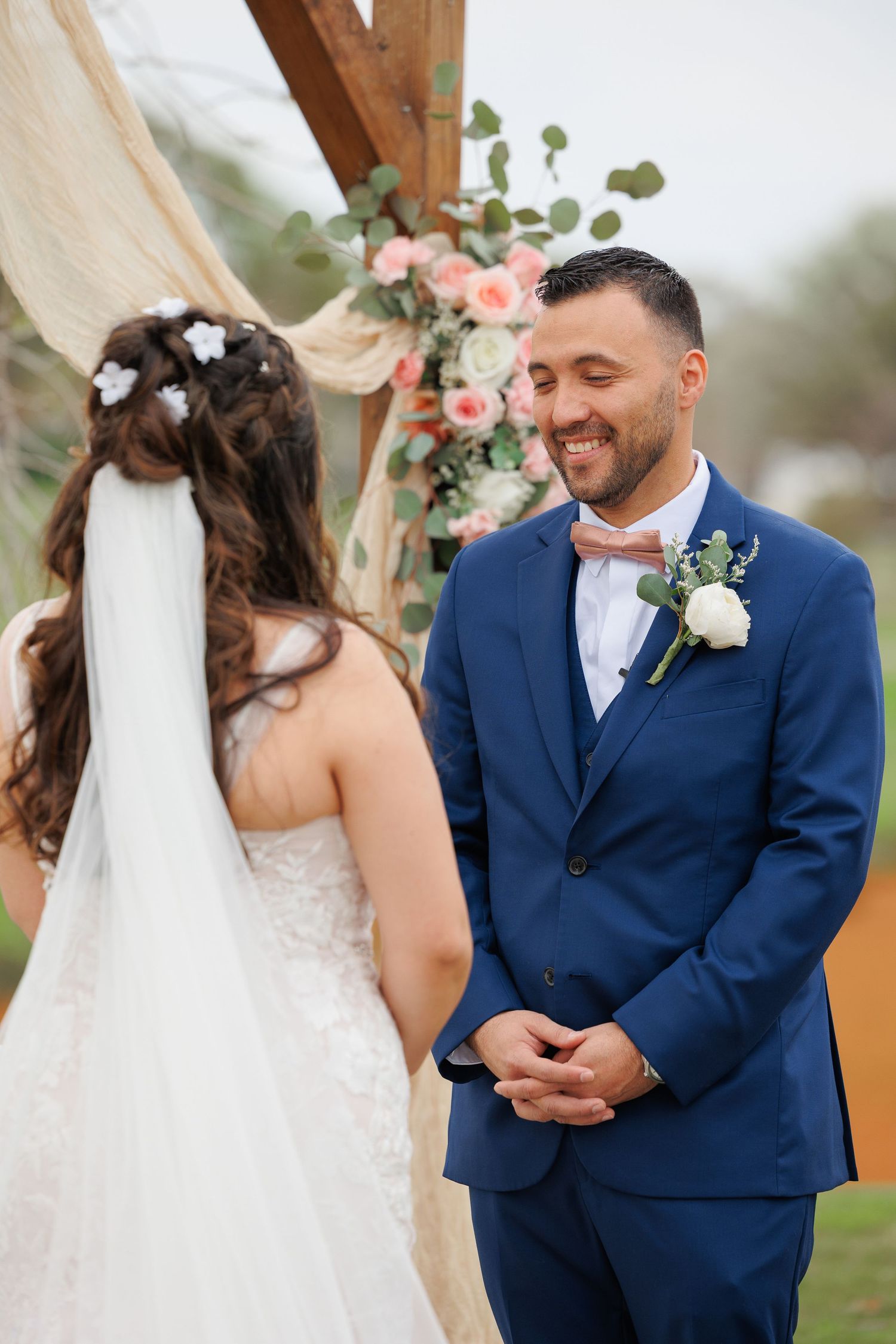 A romantic outdoor wedding ceremony with floral decor and a couple exchanging vows under a wooden arch.