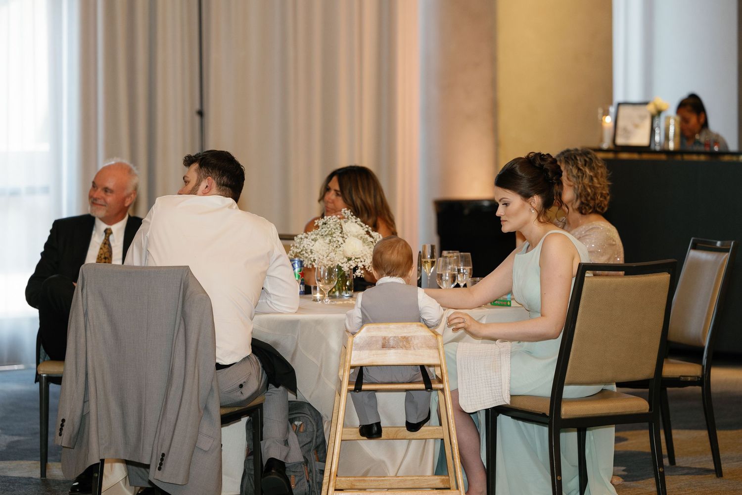 Elegant dining room with white tablecloths and guests seated at multiple tables during a formal event.