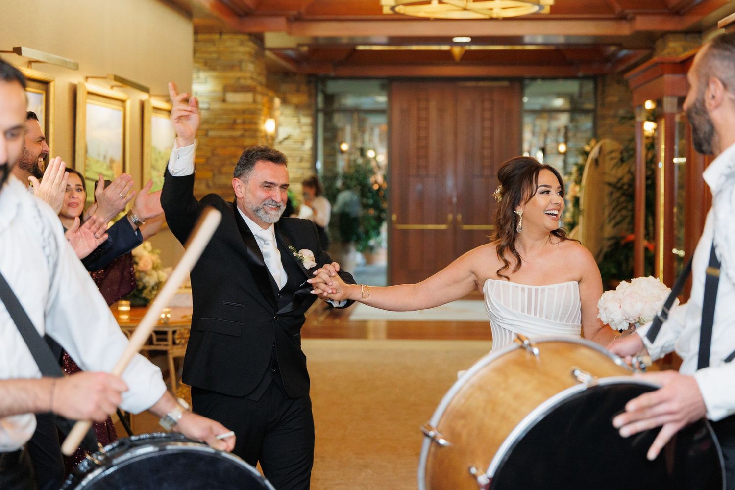 Wedding party dancing in a ballroom during a reception celebration with warm lighting and formal attire.