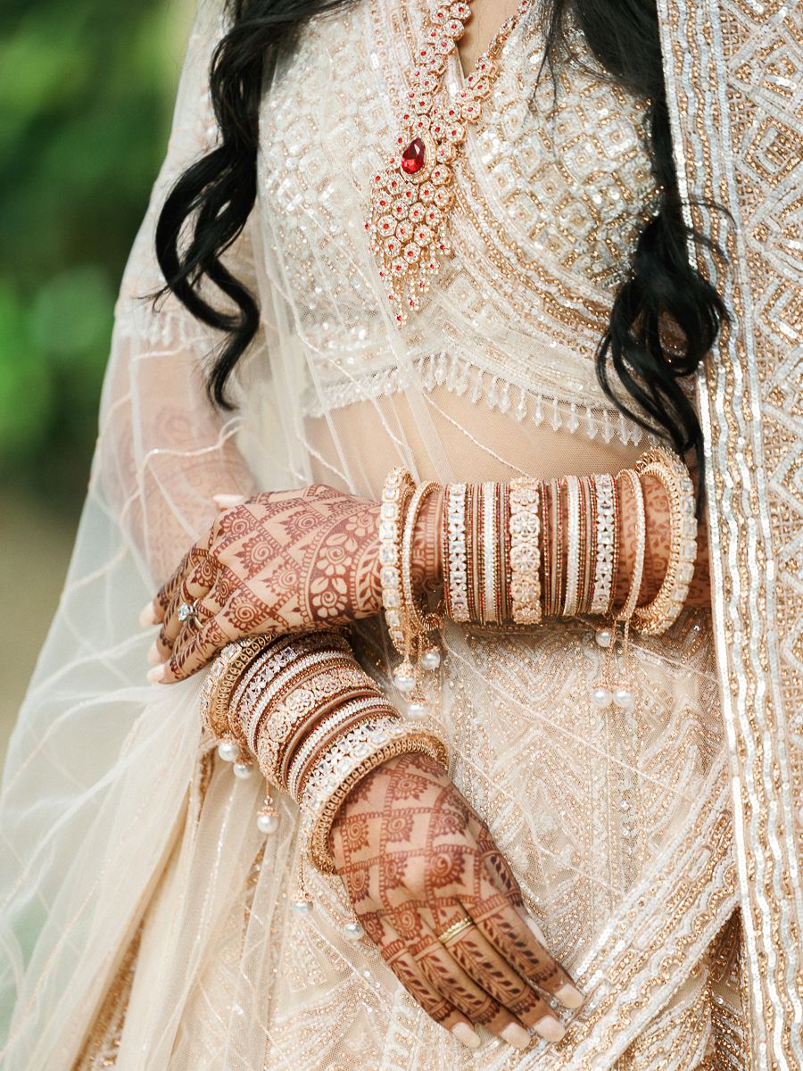Detailed view of traditional bridal mehndi and bangles with intricate beaded dress details.