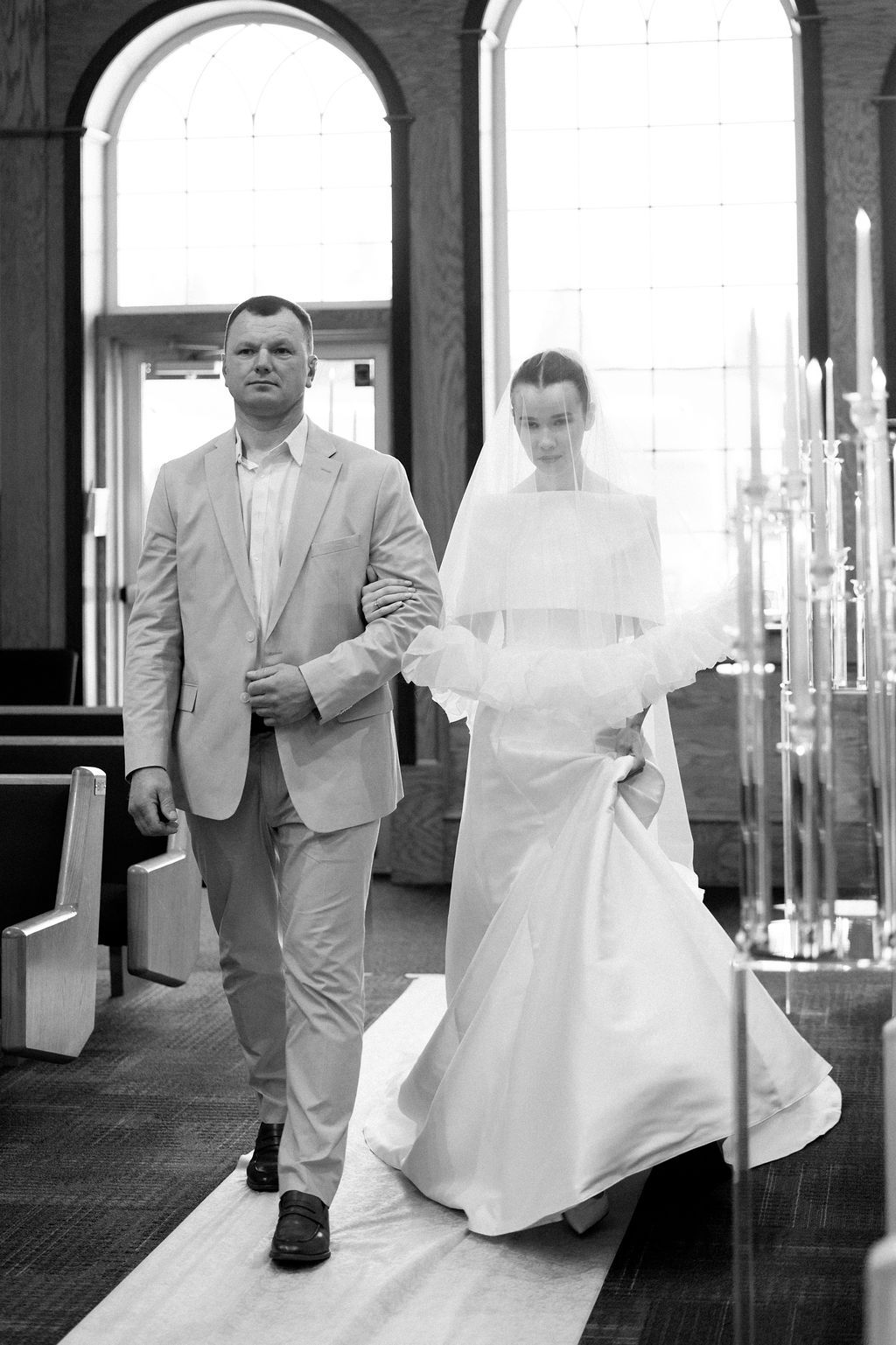 Black and white wedding photos showing a couple walking through an elegant hallway with arched windows.