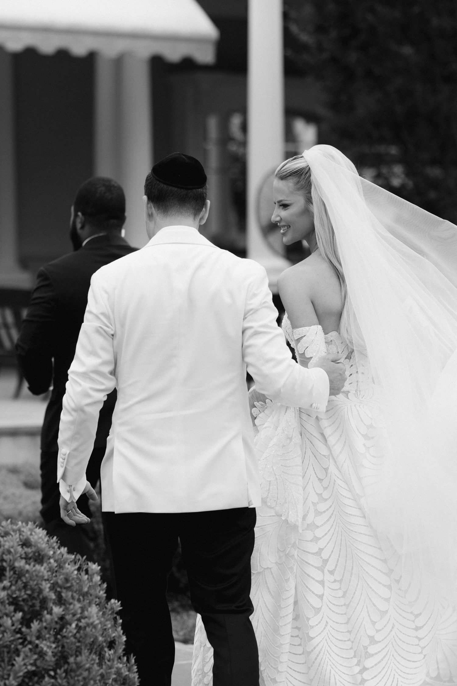 Black and white photo of a wedding party walking together, with the bride's white dress trailing behind.