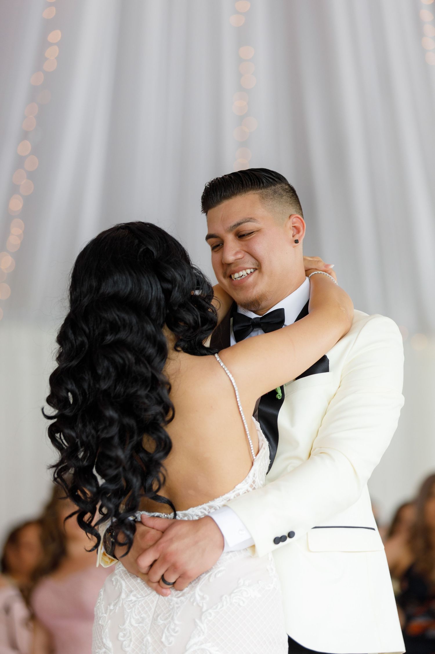 A bride and groom share their first dance at their wedding reception with romantic lighting and decor in the background.