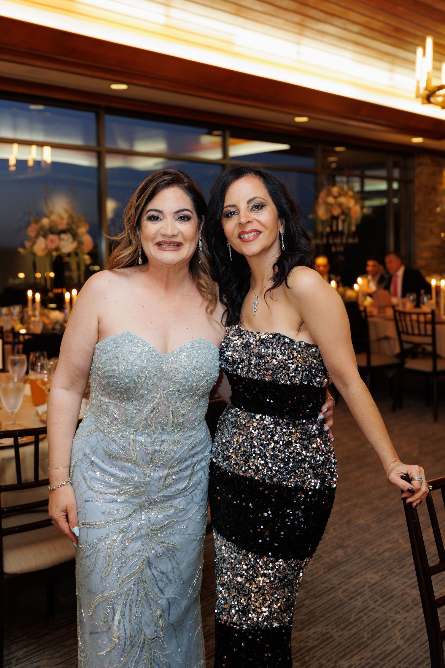Two people in formal attire, one wearing a sparkly black dress and one in a light blue gown, posing together at an event.