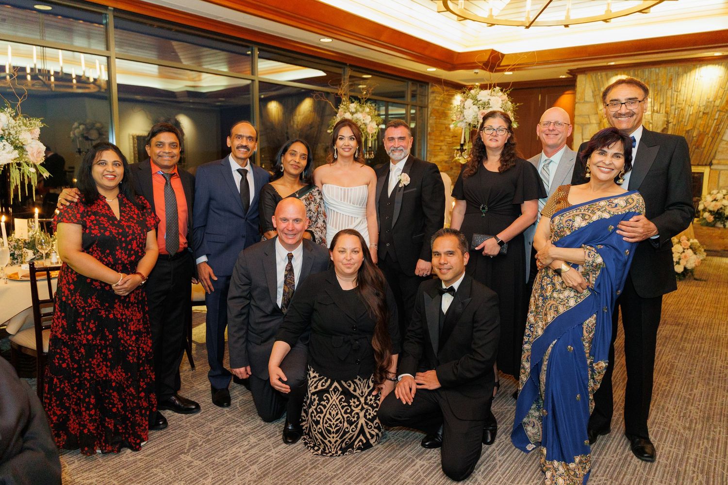 Group of elegantly dressed people gathered at a formal event in a banquet hall with ornate lighting and decor.