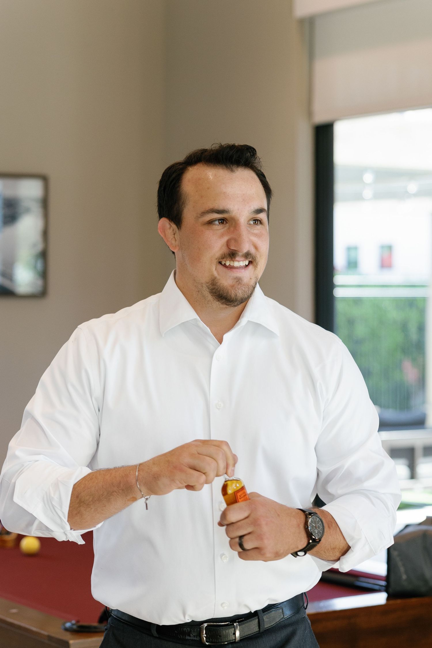 Professional in a white button-down shirt smiles while seated at a table in an office setting.