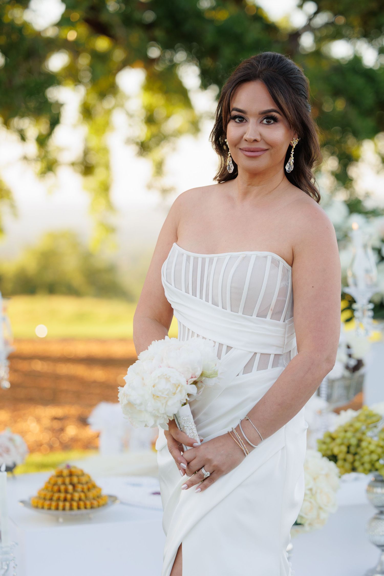 A bride in a white dress with illusion stripes poses outdoors during golden hour with floral decorations.