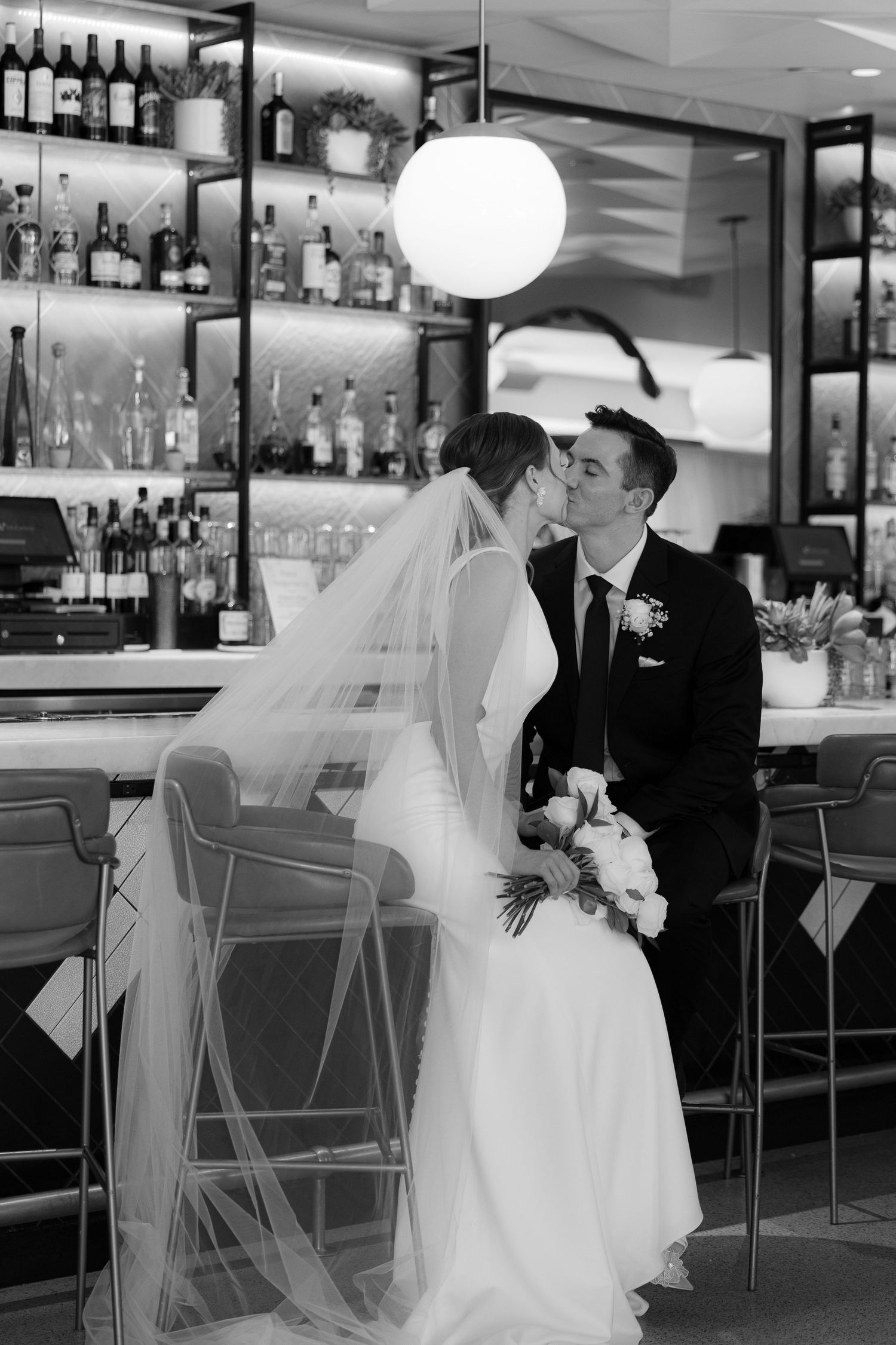 A romantic black and white photo series of a bride and groom sharing intimate moments at a bar counter.