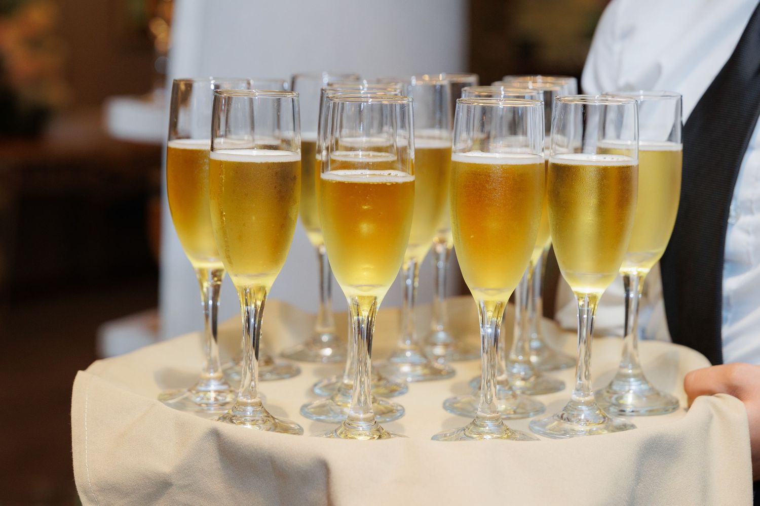 Champagne flutes filled with golden bubbly beverages arranged on white linen cloth at formal event service.