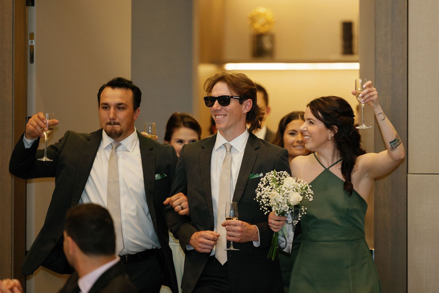 Wedding guests raise their glasses in a toast during an indoor reception celebration.