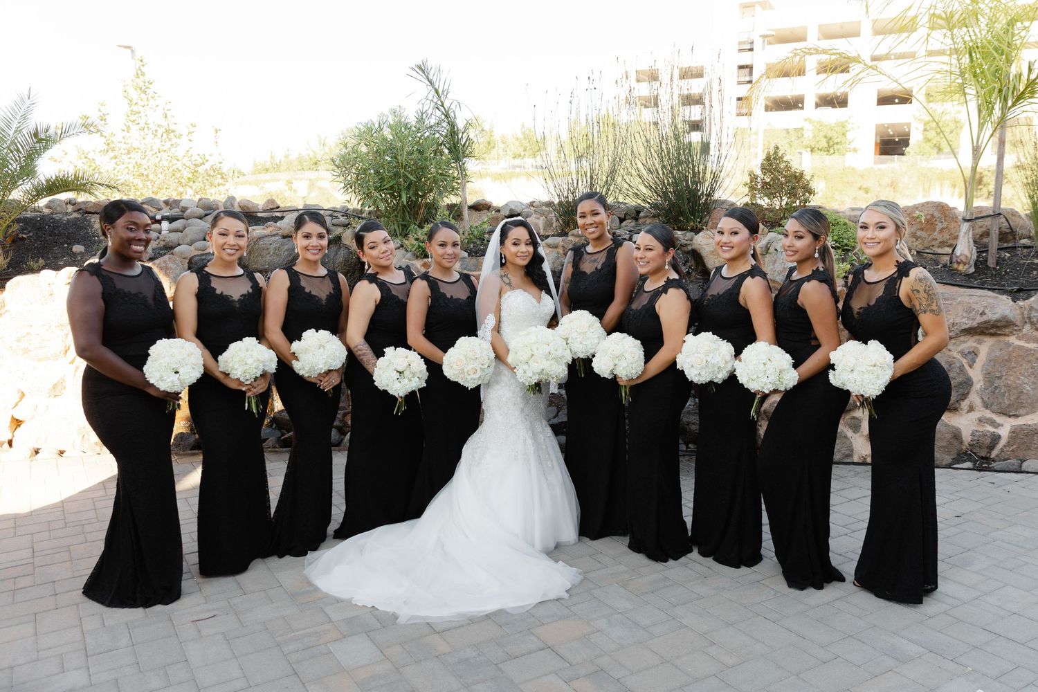 Wedding party wearing black and white formal attire poses together for group photos on stone steps outdoors.