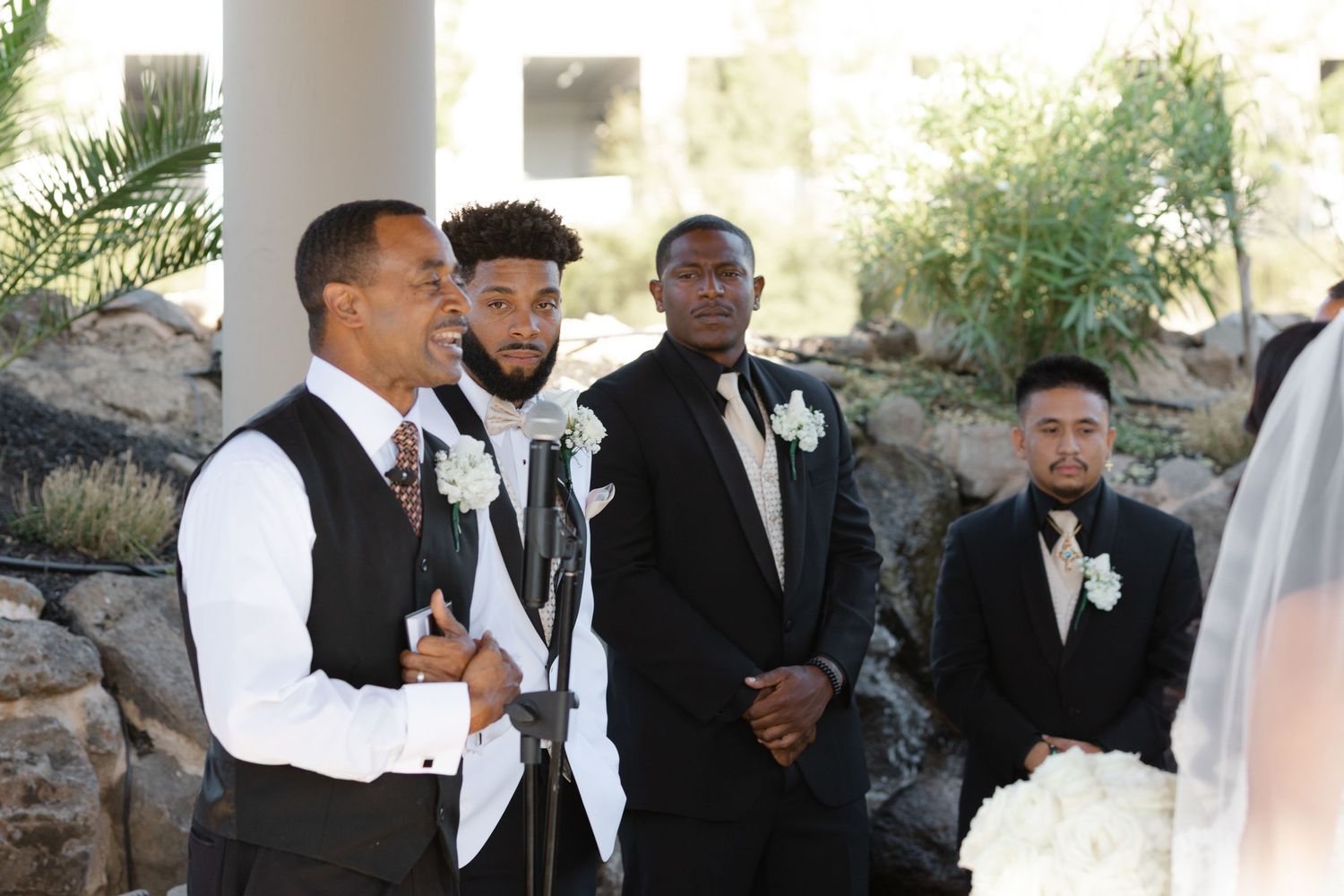 Wedding party members in black and white formal attire stand together during an outdoor ceremony.