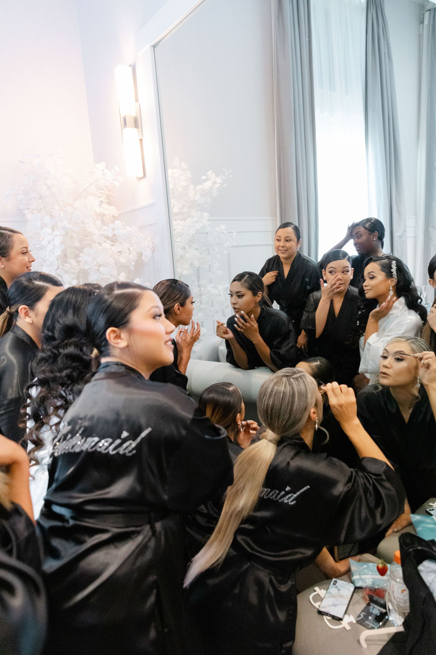 A group of people in matching black satin robes prepare for an event in a bright room.