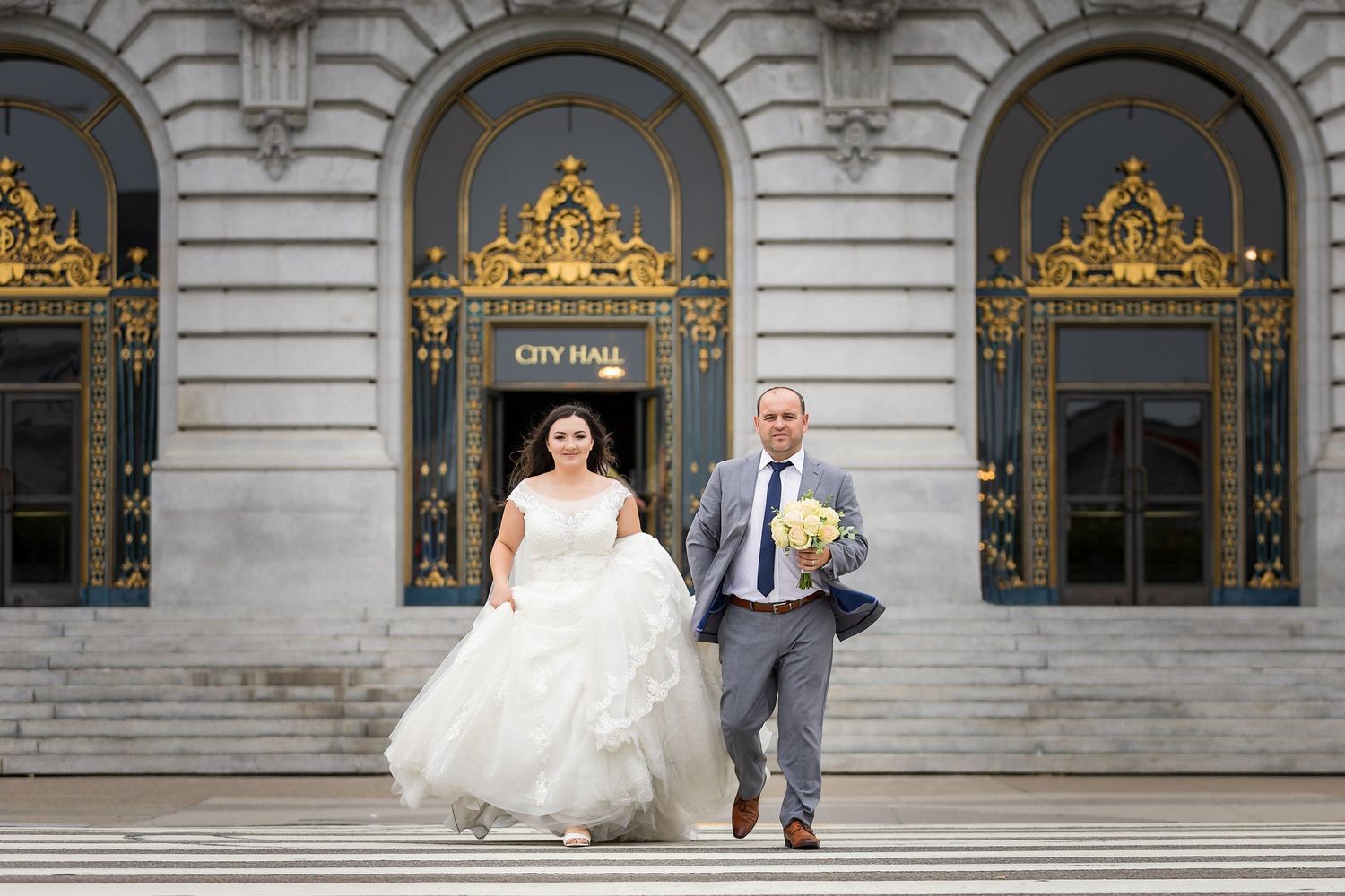 Bride and groom descending steps of San Francisco City Hall after wedding ceremony.