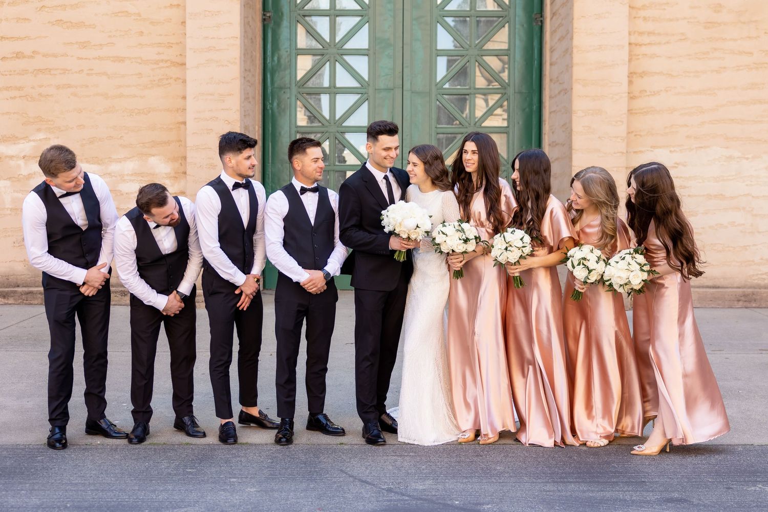 Wedding party in formal attire with bridesmaids in pink dresses and groomsmen in black vests.