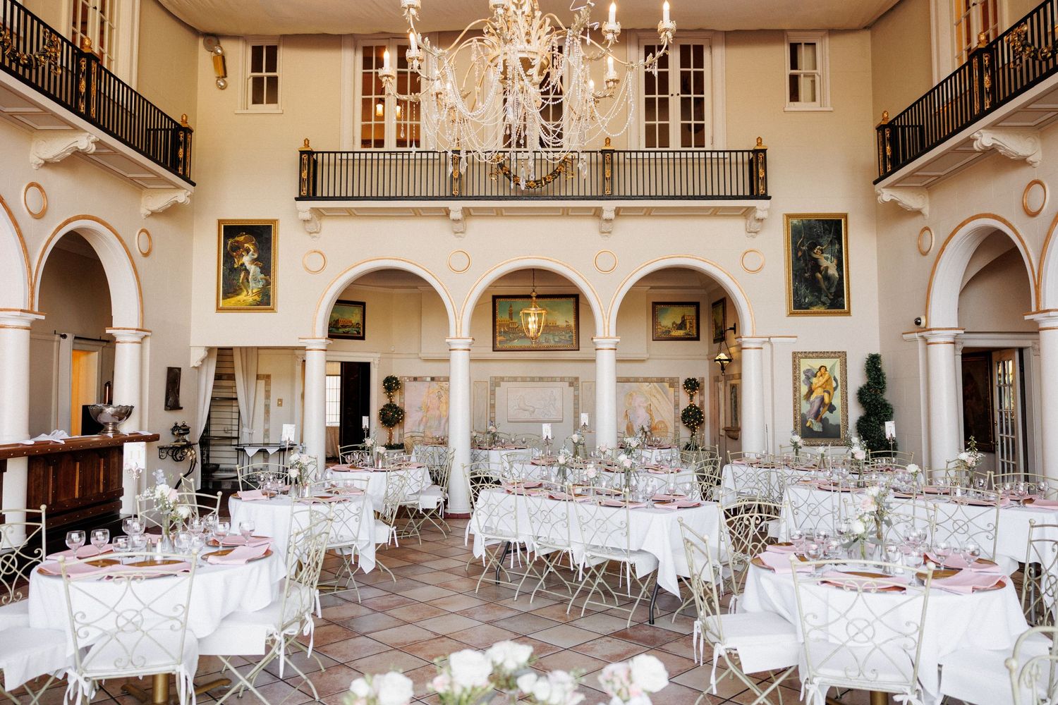 A panoramic view of an elegant wedding reception venue with crystal chandeliers and white-clothed tables in a grand ballroom.