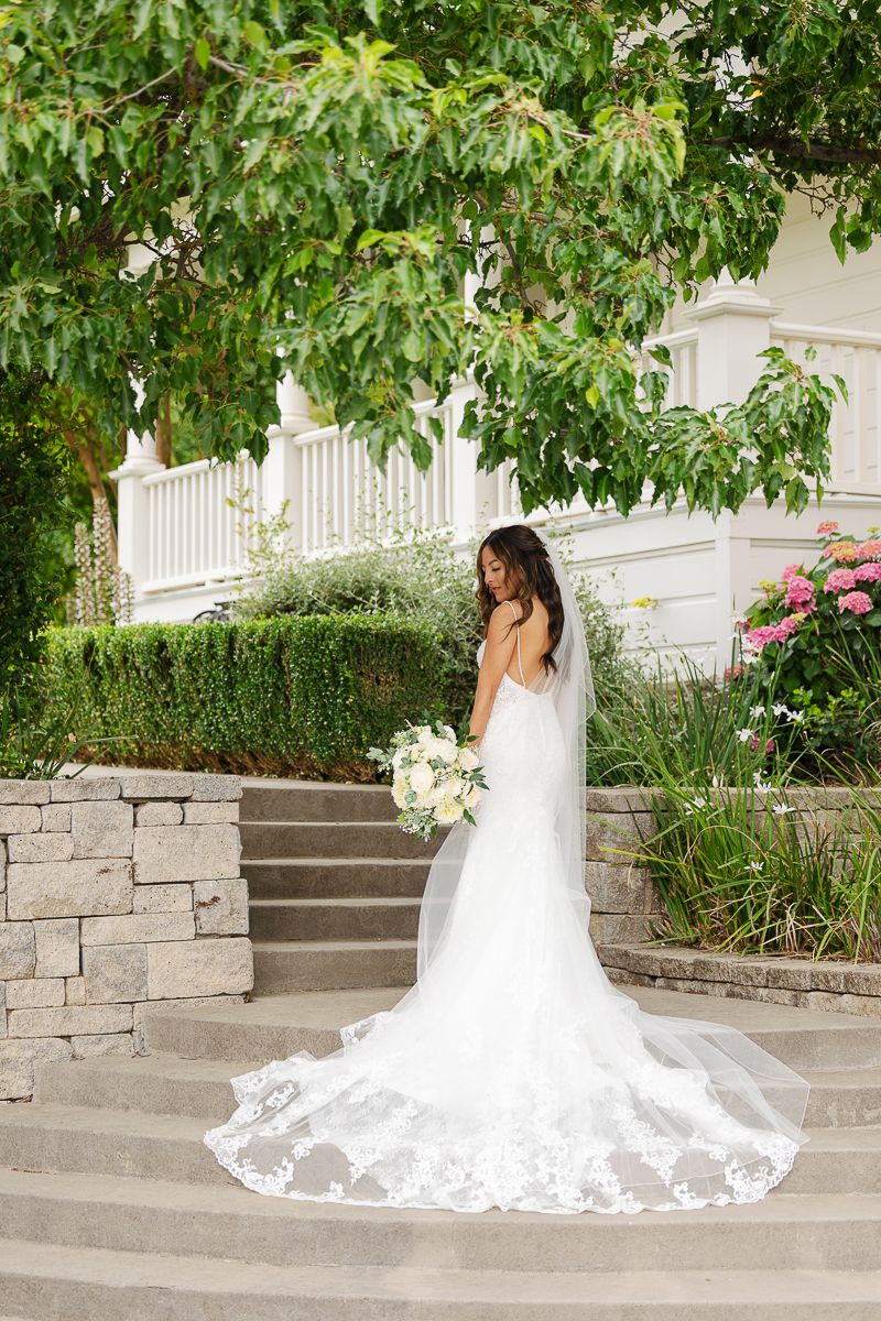 A stunning wedding dress with a long lace veil cascades down stone steps in a garden setting.