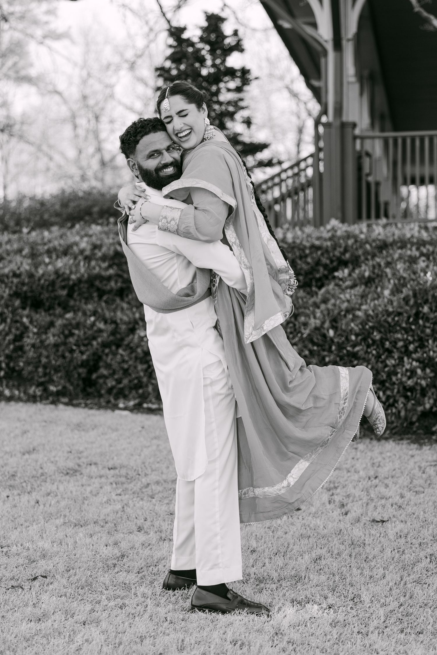 Black and white portrait of a joyful couple embracing outdoors, with one person lifting the other in a playful moment.