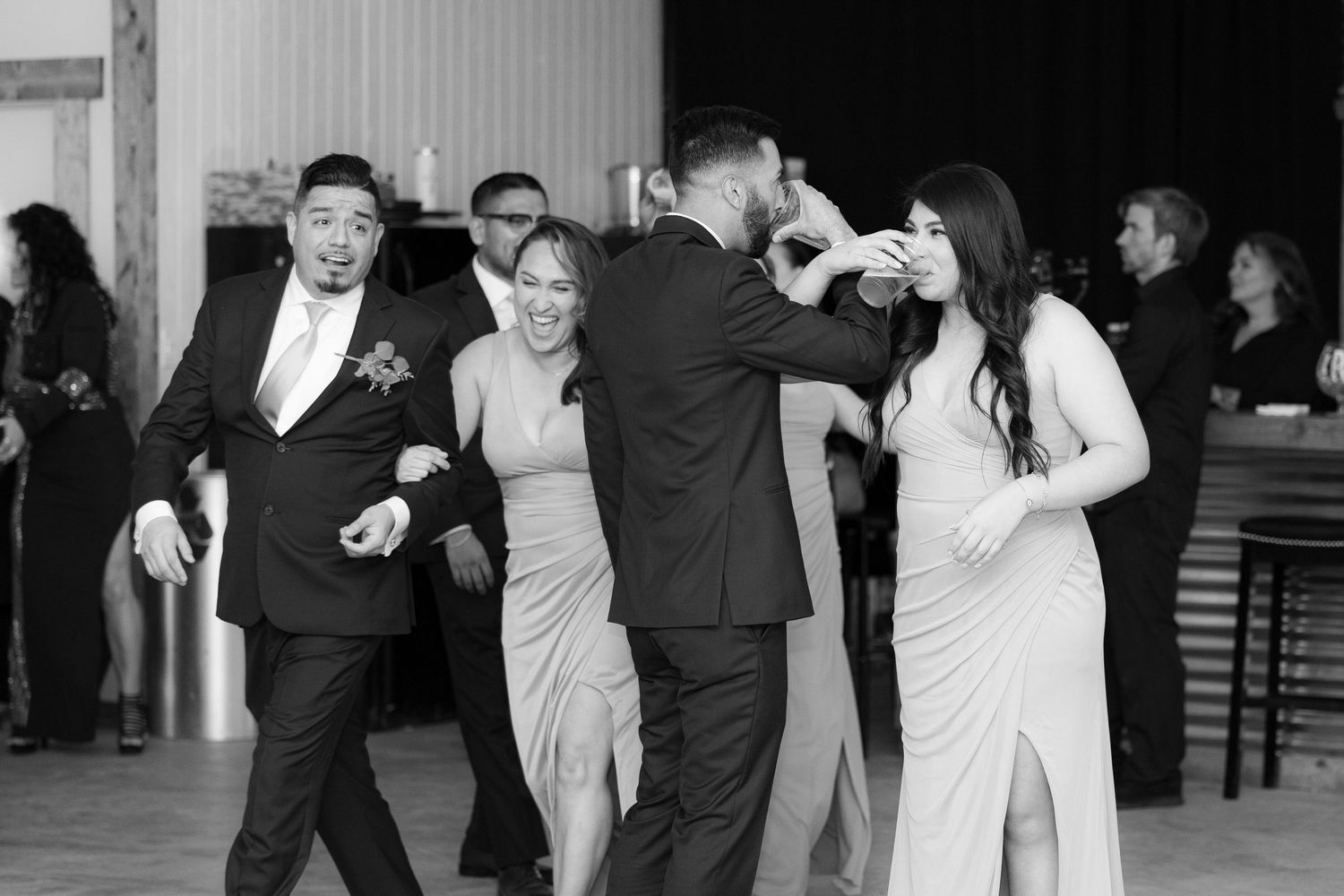Wedding party members laugh and dance together during a fun reception celebration in black and white.