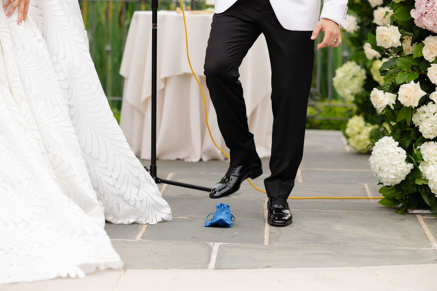 Wedding couple's feet shown at ceremony with white dress, black suit pants and blue tennis shoe detail against floral backdrop.