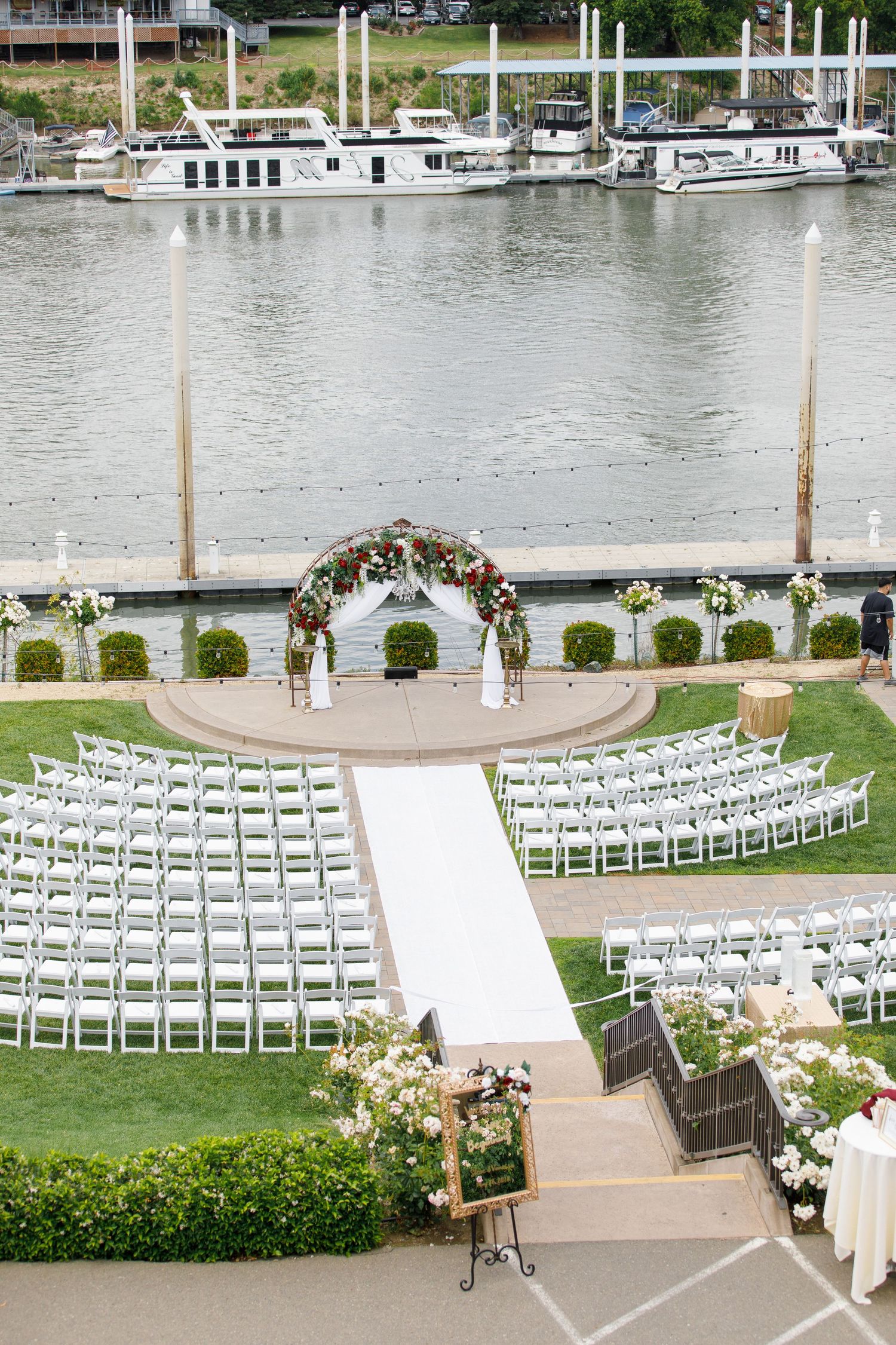 White chairs arranged in curved rows for an outdoor waterfront wedding ceremony with floral decorations and a marina backdrop.