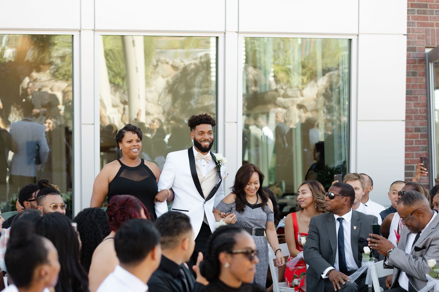 A crowd of people gathered outside a building with glass windows and brick walls during a social event.