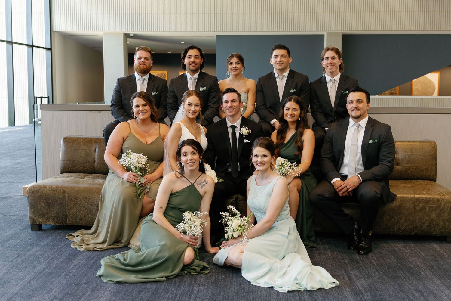 Wedding party members sit casually on modern gray steps in formal attire during a relaxed photo session.