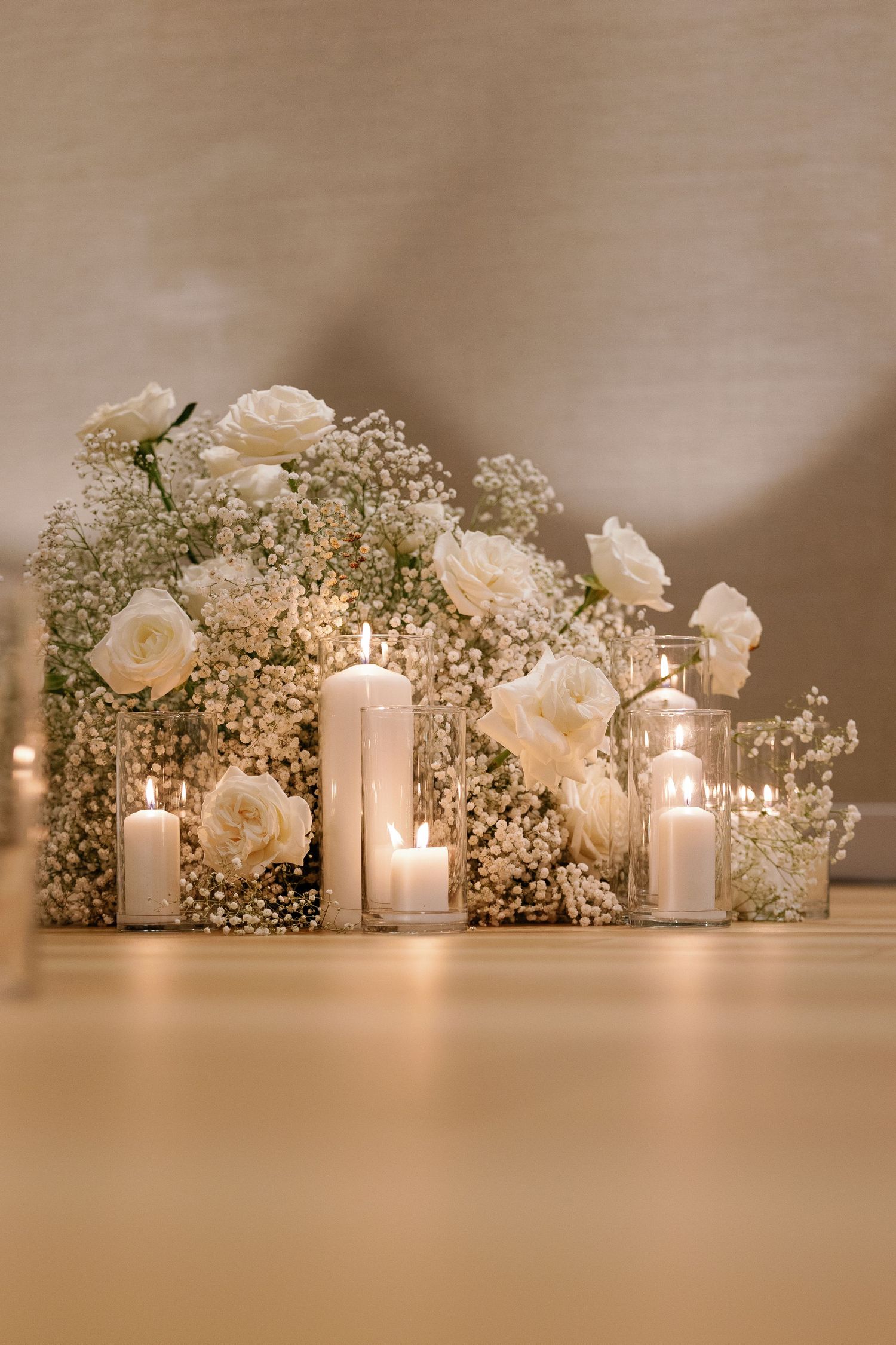 Elegant wedding table decor with glowing candles in glass holders surrounded by white roses and baby's breath flowers.