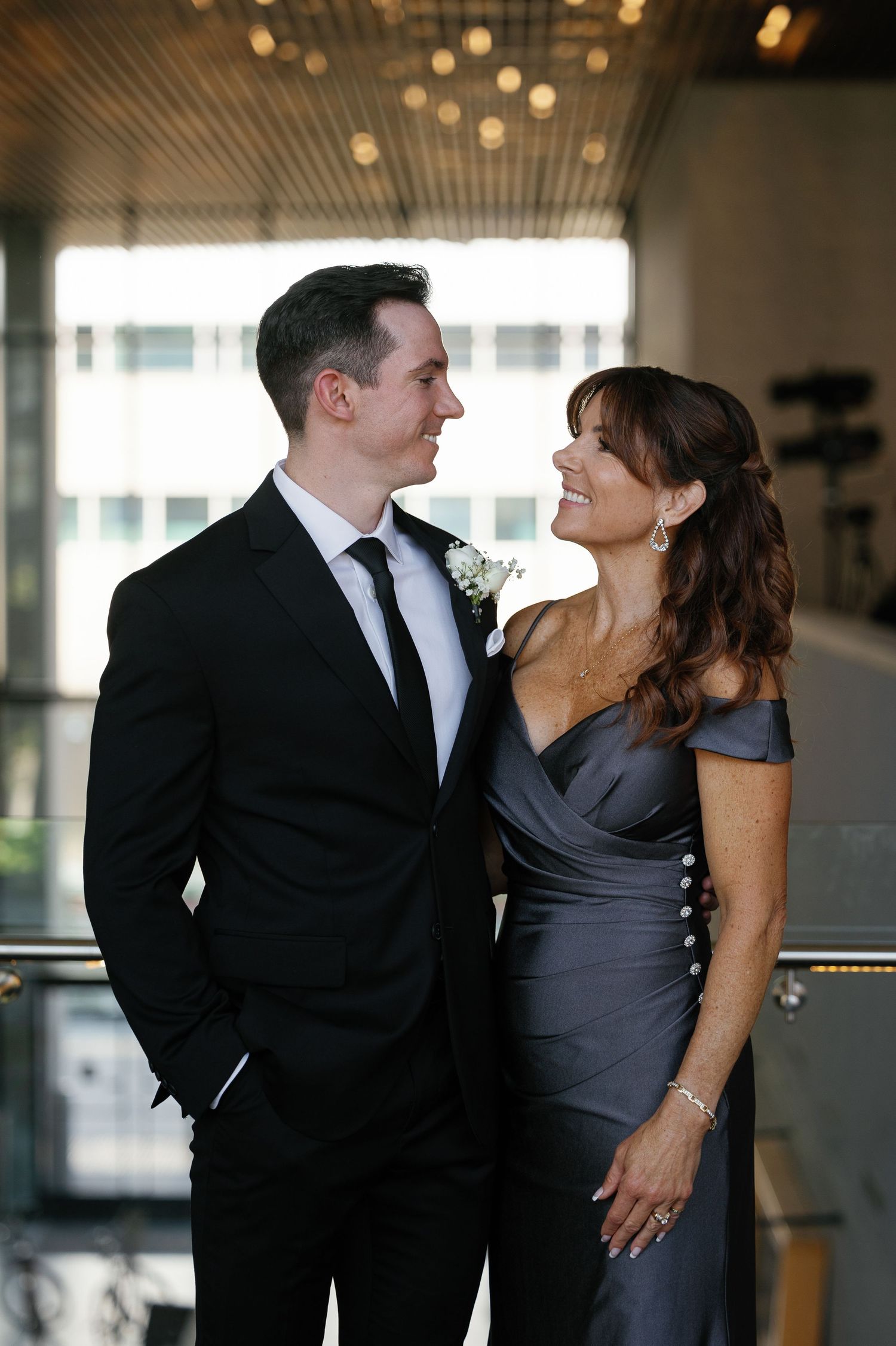 Elegant couple in formal attire share a romantic moment in a modern indoor setting with soft lighting.