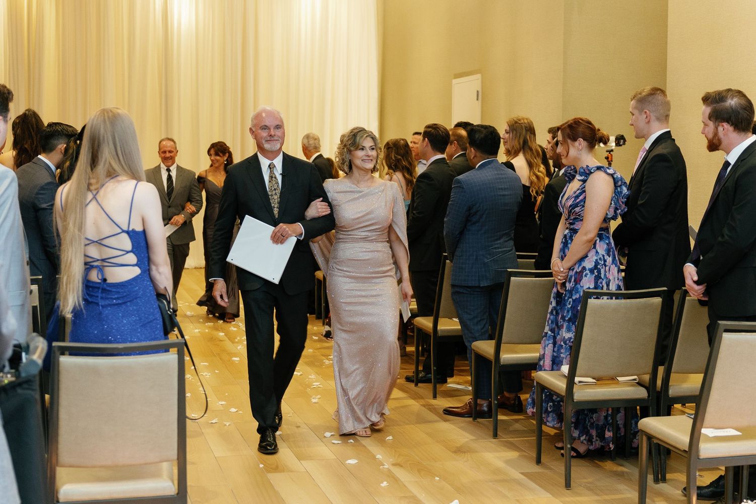 A panoramic view of a formal event in an elegant ballroom with guests mingling and seated at round tables.