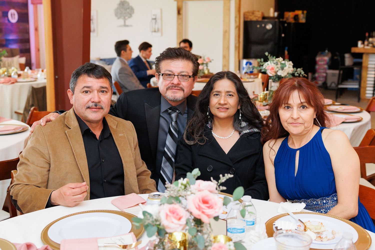 Four guests smile together at a formal dinner event with pink floral centerpieces on the table.