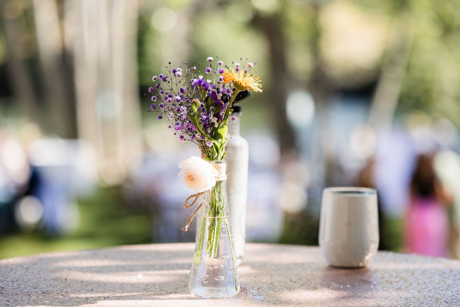 Delicate wildflowers in glass vases decorate a rustic outdoor table setting for a garden party.