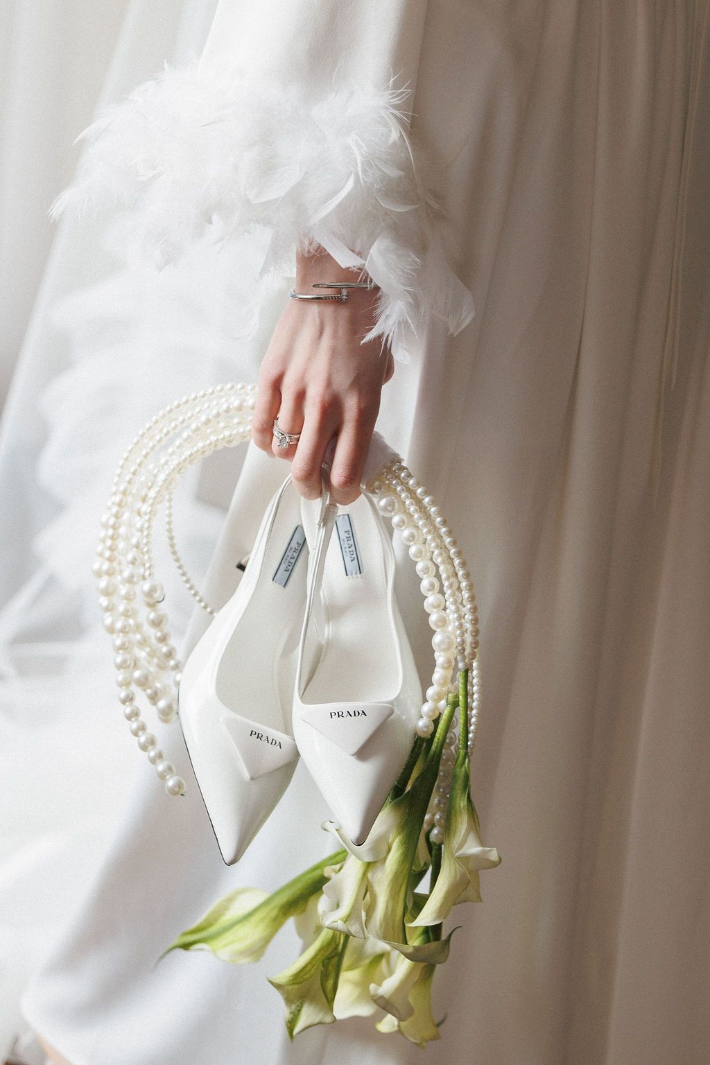 Pearl-handled bridal bouquet with white Prada heels and green stems arranged on white tulle fabric.