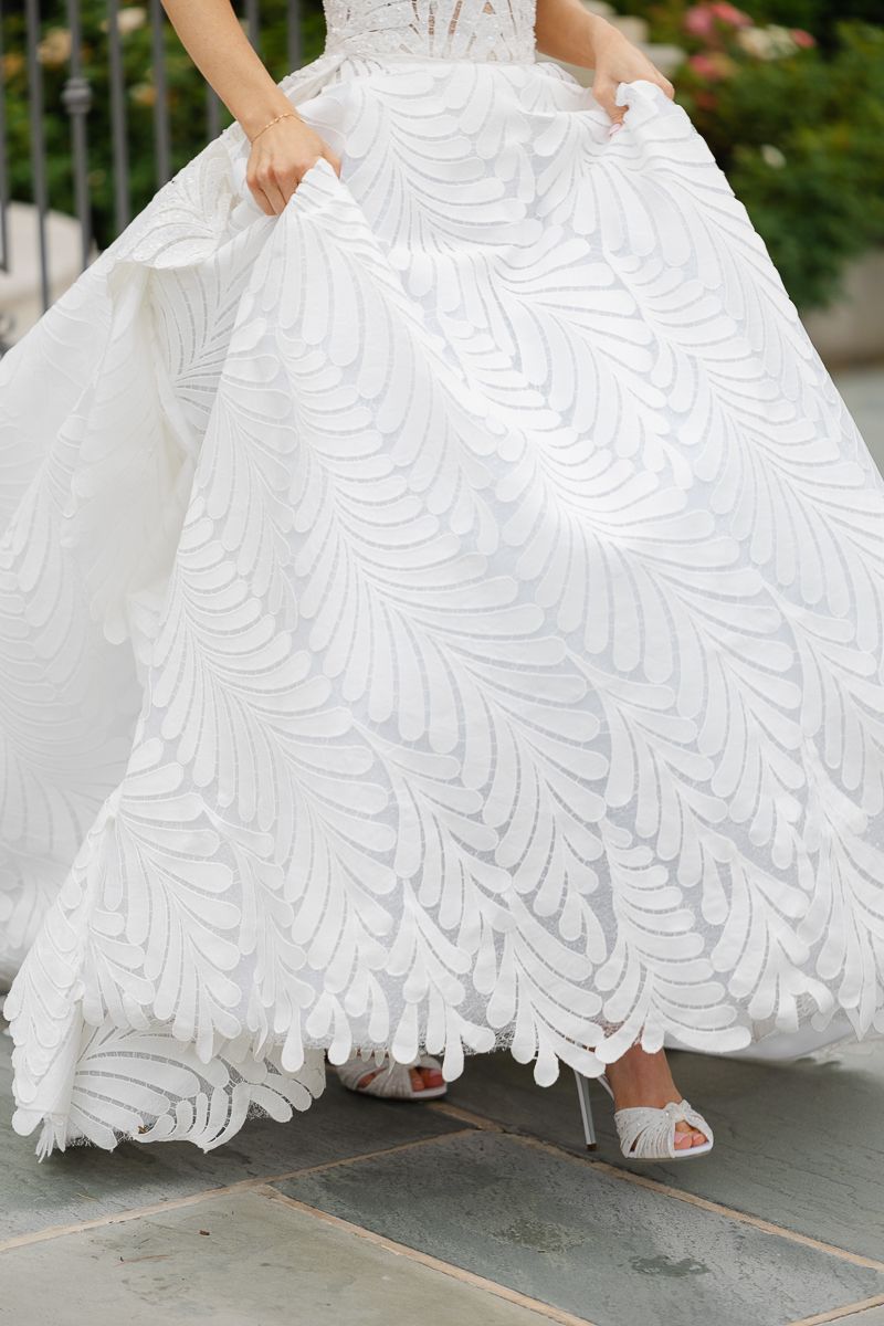 Close-up shots of an elegant white wedding dress with intricate lace details and feathered patterns.