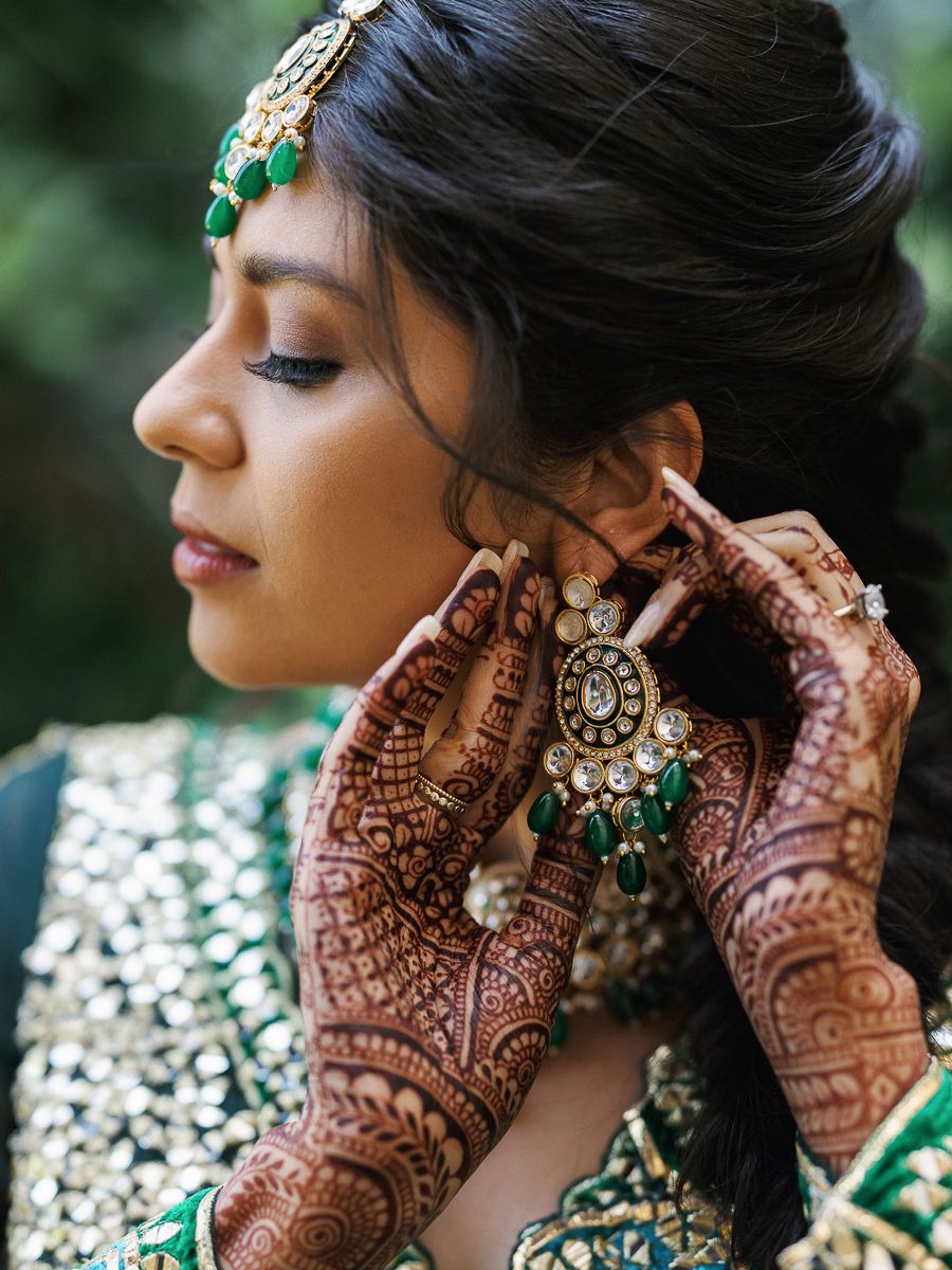 Traditional Indian bridal jewelry and intricate henna designs on hands showcased with emerald and gold accessories.