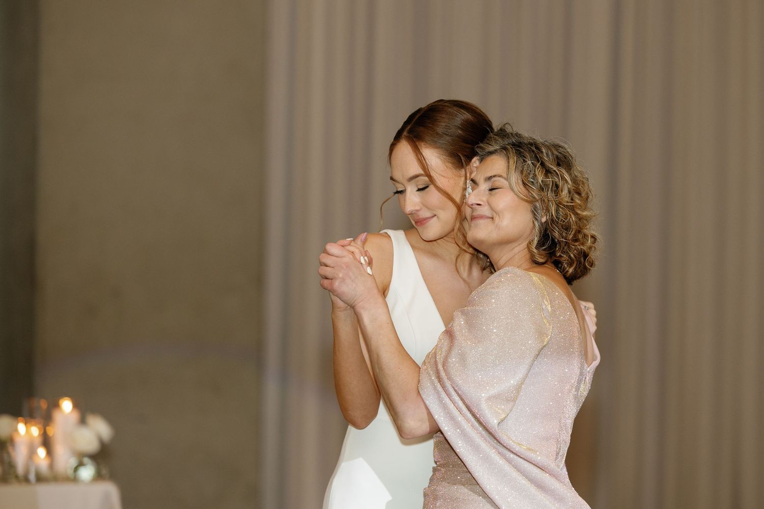 Two people share an intimate dance moment together in formal attire with candlelight in the background.