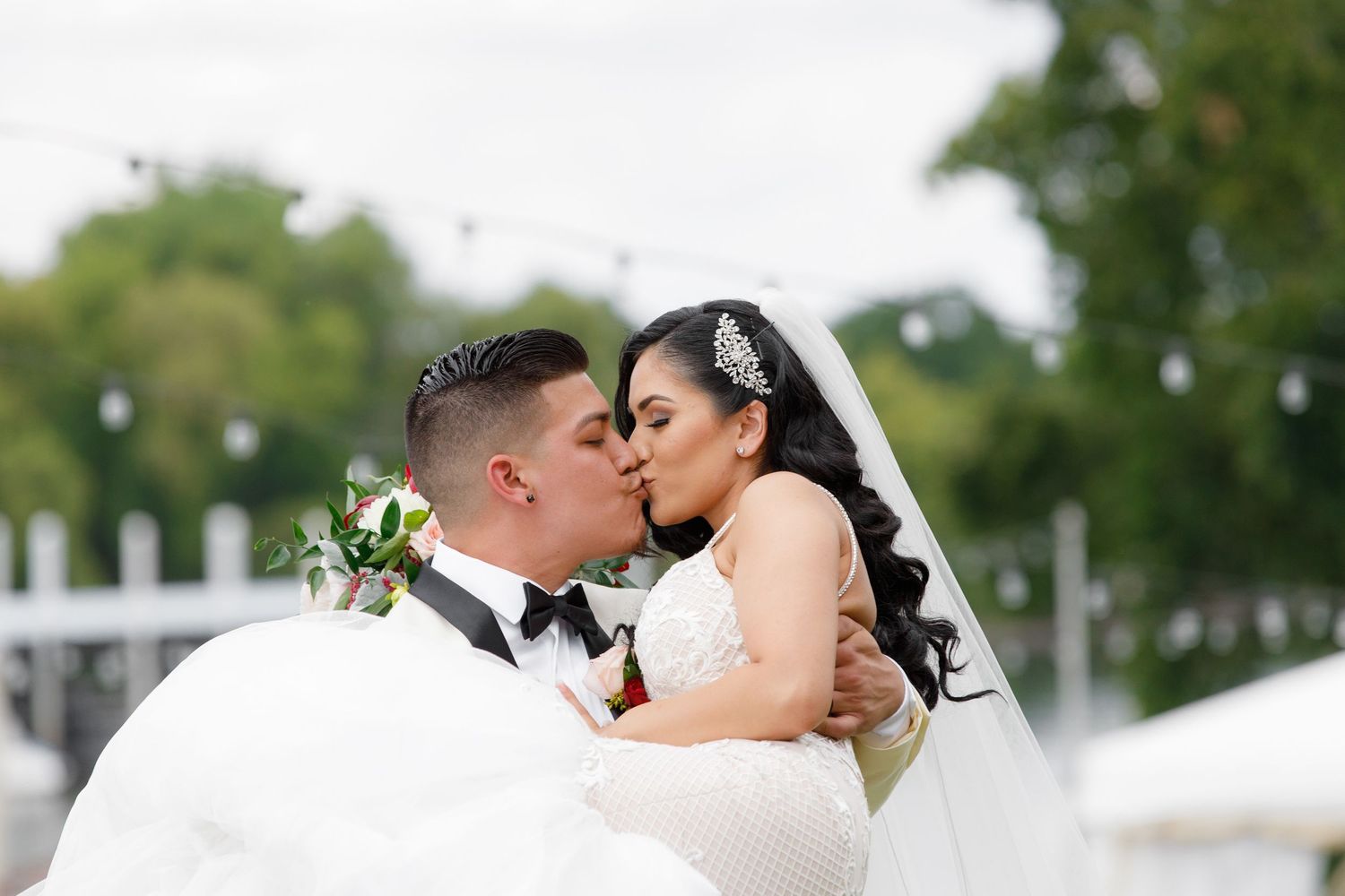 A romantic wedding couple shares a tender kiss during an outdoor ceremony with lush greenery in the background.