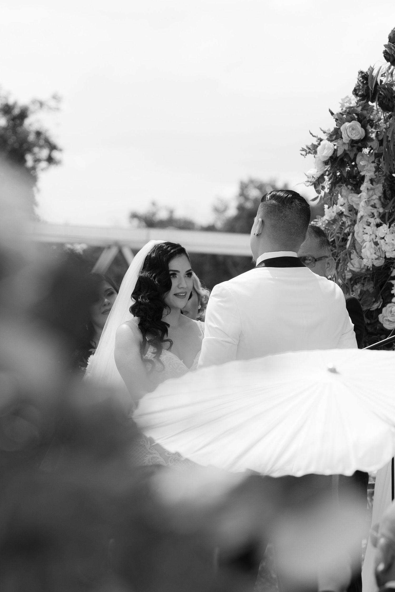 A romantic black and white wedding photo showing a couple's veil flowing dramatically in the wind during an outdoor ceremony.