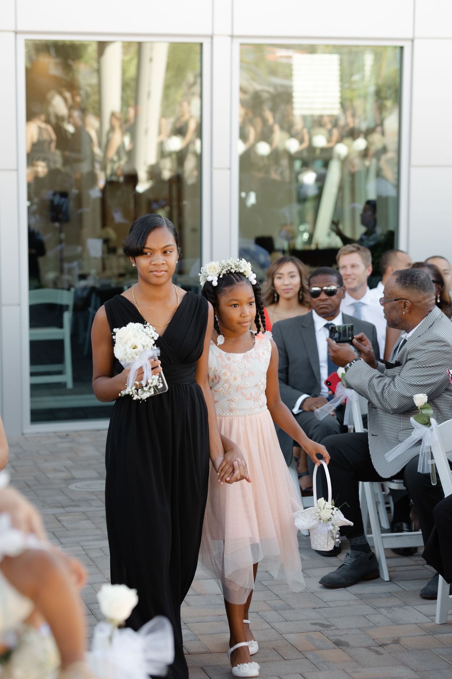 Wedding party members in black dresses and a pink dress gather on an outdoor patio during a celebration.