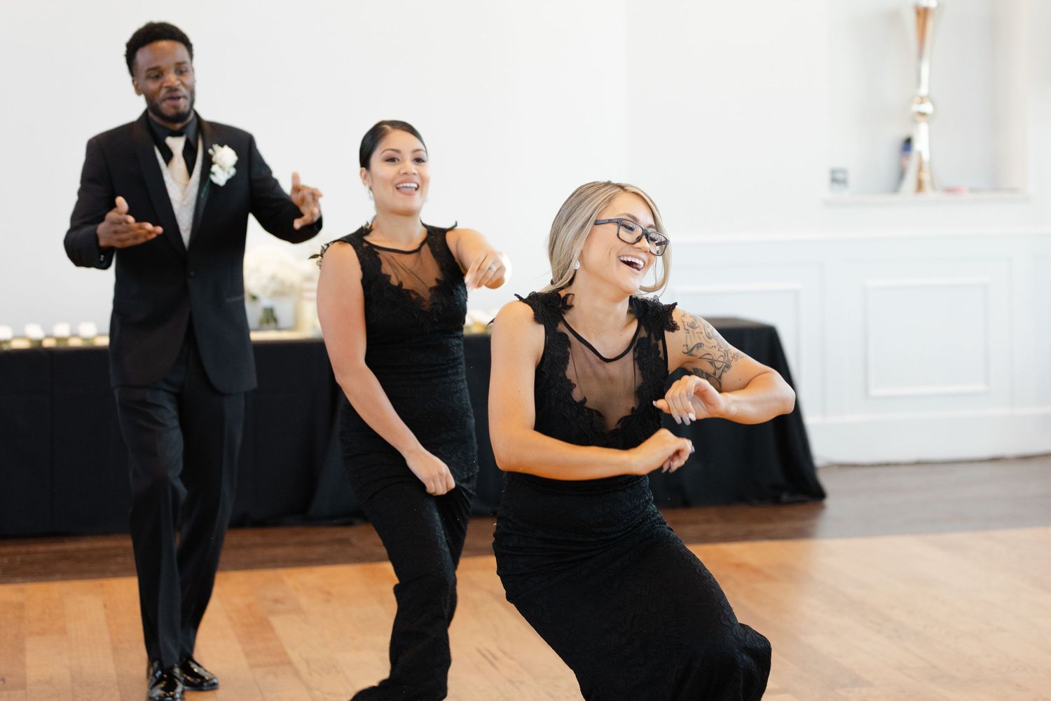 Three performers in black attire dance energetically together during a performance on a wooden floor.