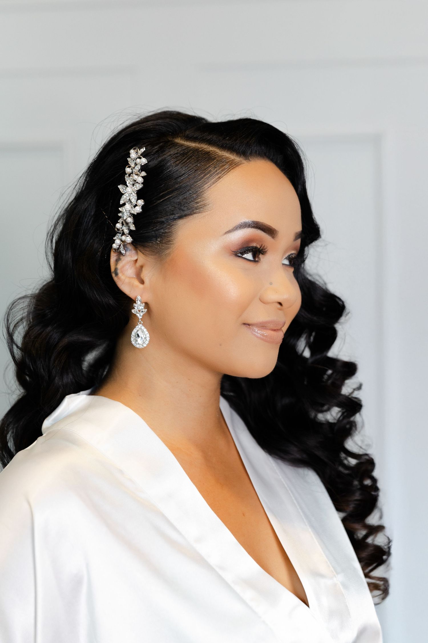 Beautiful bridal portrait showing elegant hairstyle with crystal hair accessory, dangling earrings and white silk robe.