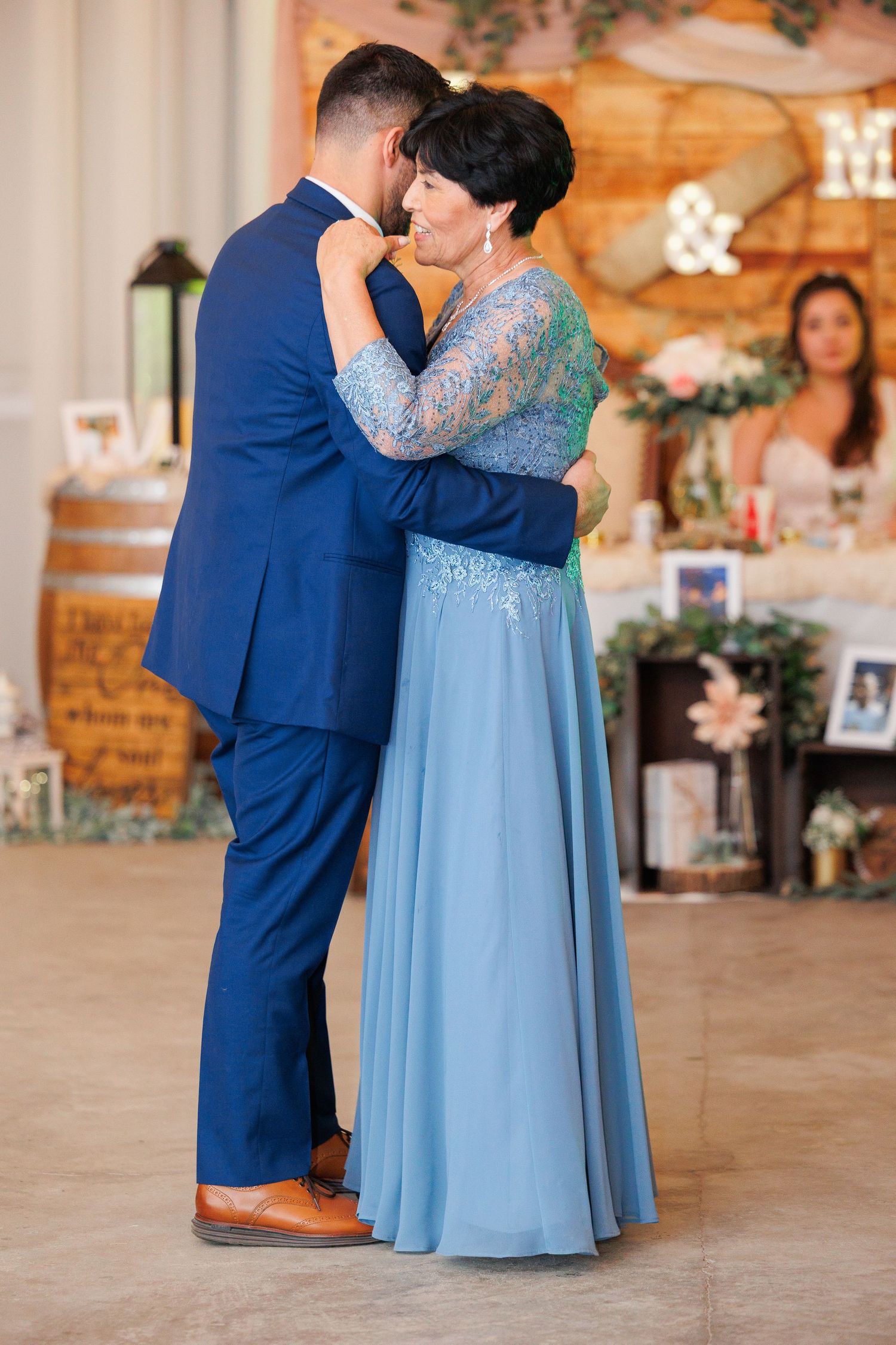 A couple shares a tender dance moment at a wedding reception, with the groom in navy blue suit and partner in light blue gown.