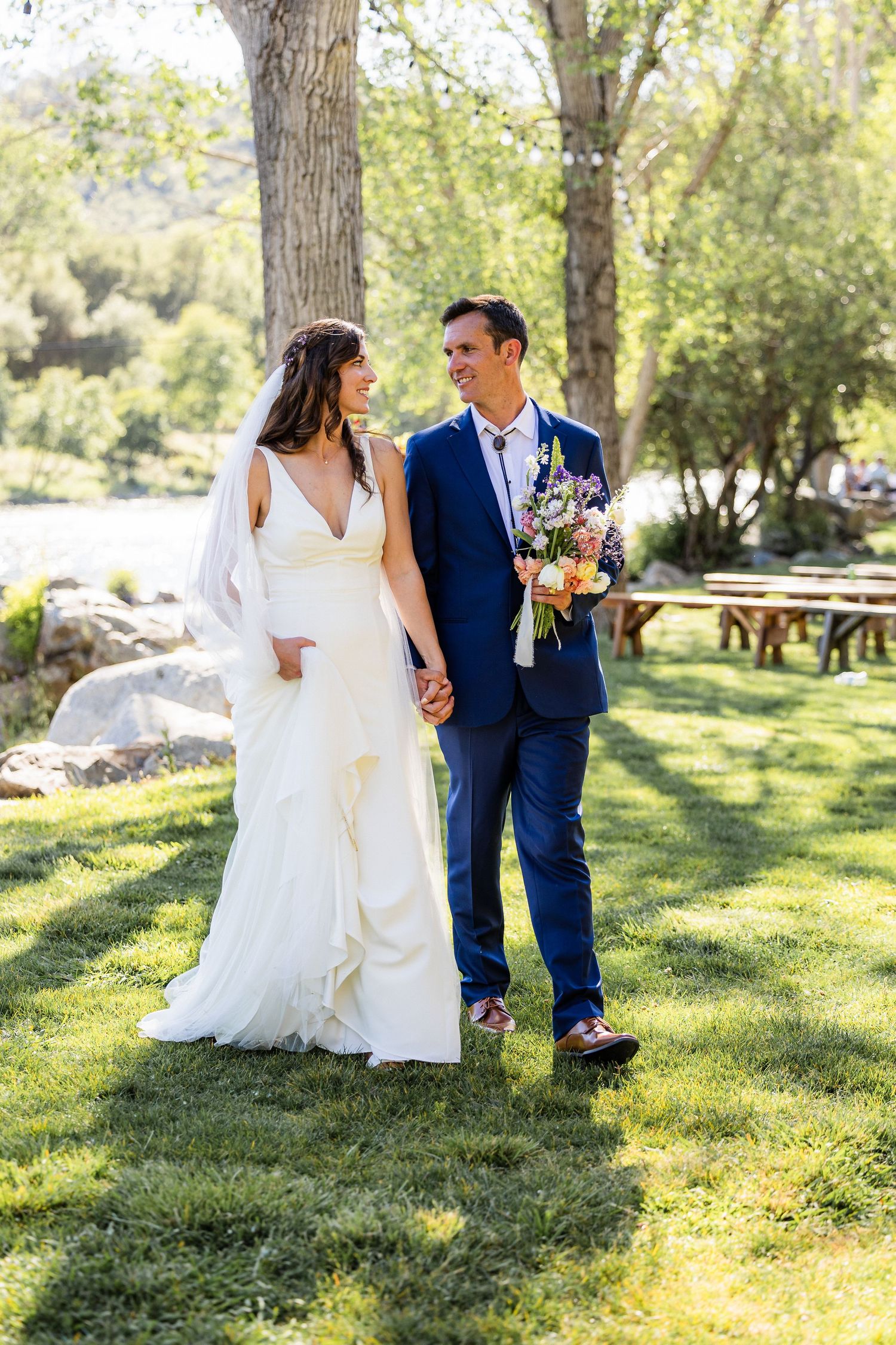 Newlyweds walk together on lush green grass in a sunlit garden setting during their wedding celebration.