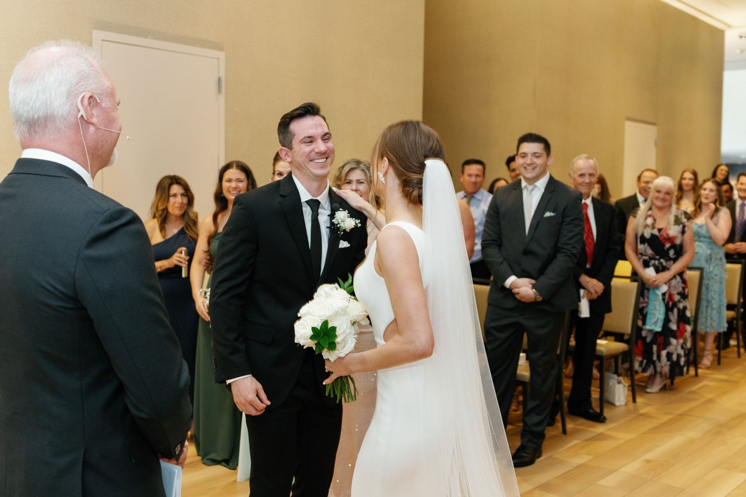 Wedding ceremony procession in bright church hall with guests watching from wooden pews.