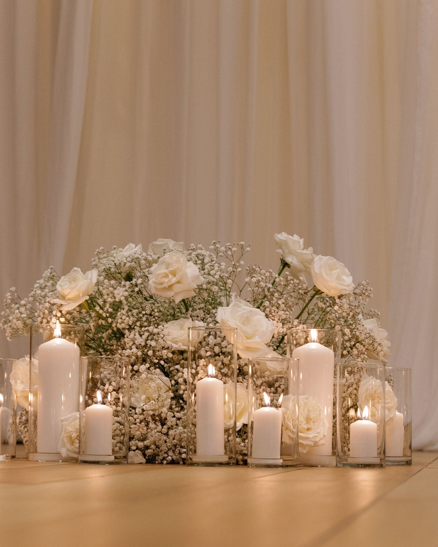 Elegant wedding reception decor with white roses, baby's breath and glowing candles arranged on a long table.