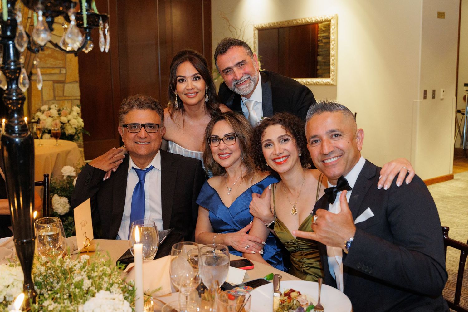 A group of people smiling and posing together at a formal dinner event with elegant table settings and decor.