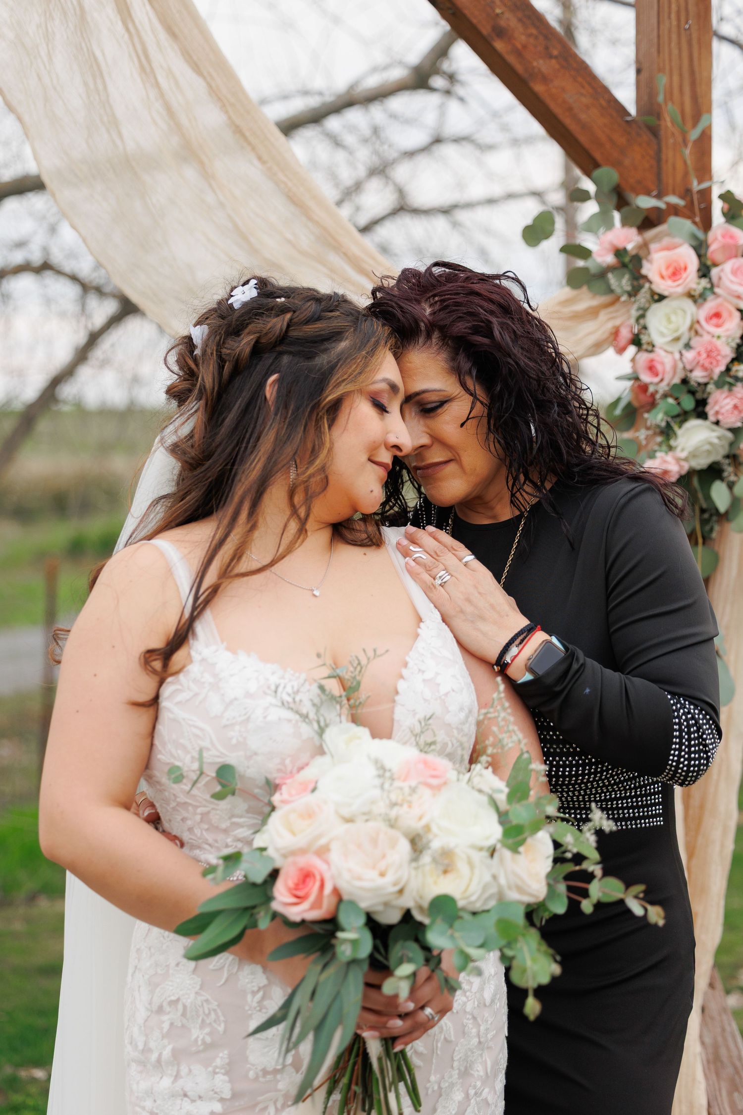 Two people share an intimate moment at a wedding ceremony under a floral arch with pink and white roses.