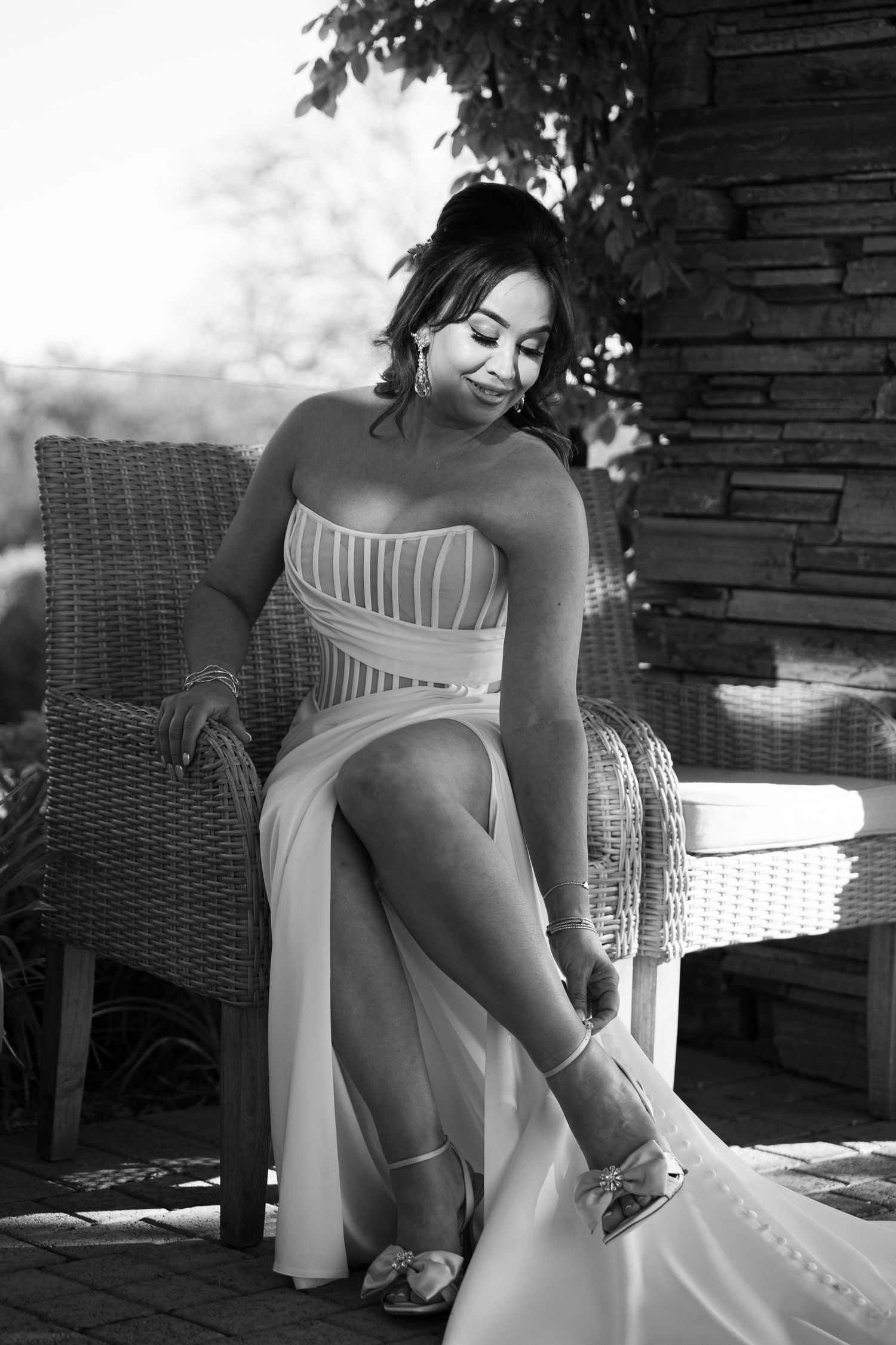 Black and white portrait of someone in an elegant white dress sitting in a wicker chair outdoors.
